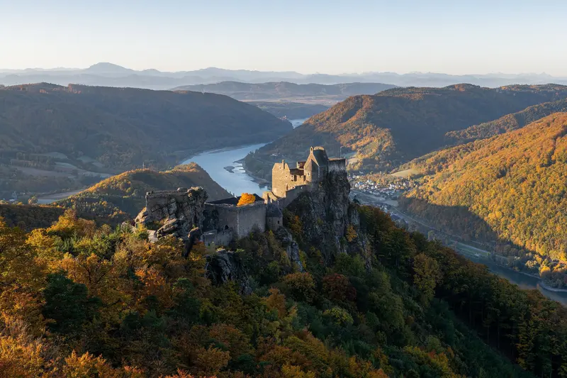 Die Burgruine Aggstein auf ihrem Felsen im Herbstlicht, dahinter die Donau zwischen bewaldeten Hügeln
