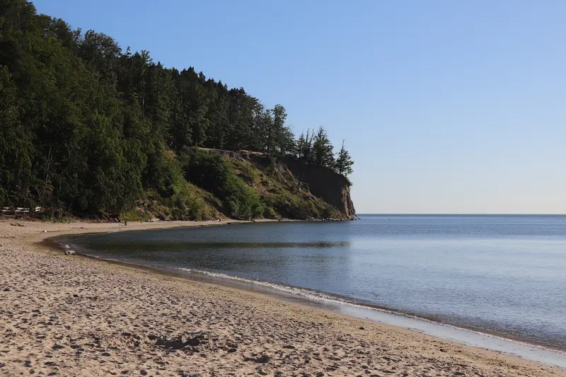Ein leerer Strand in Orłowo am Morgen, dahinter das bewaldete Kliff über der ruhigen Ostsee