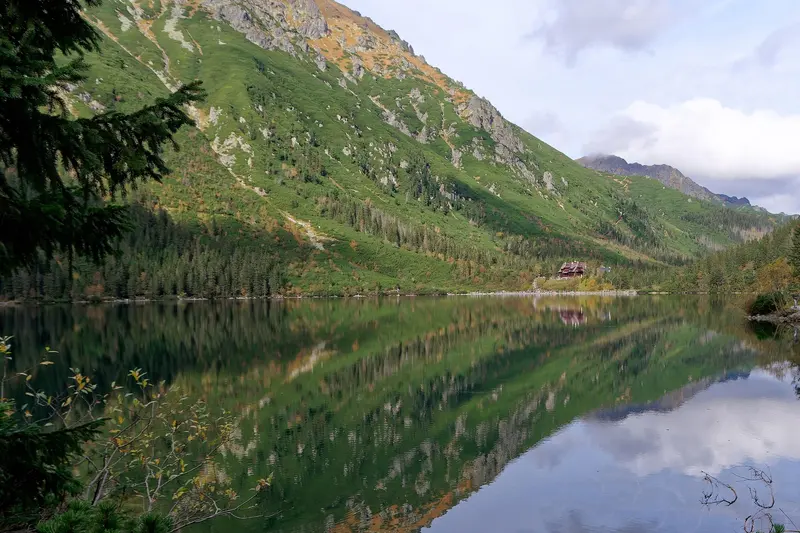 Morskie Oko im Herbst, mit der Berghütte am anderen Ufer und den Gipfeln im Wasser gespiegelt